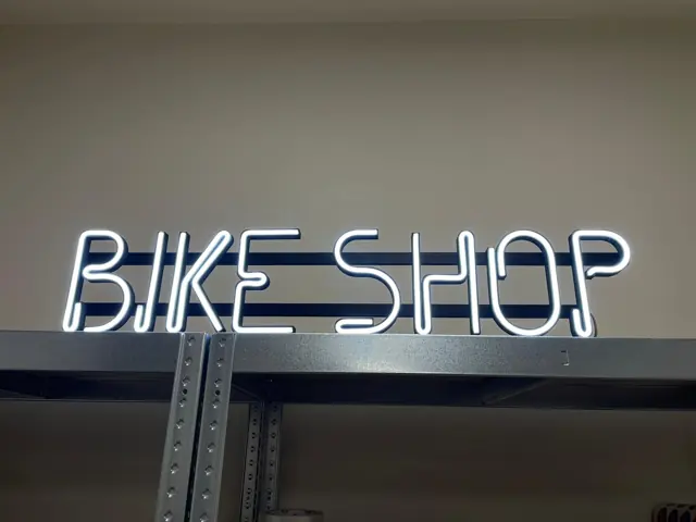 Baltas LED neoninis užrašas „Bike shop“ ant lentynos